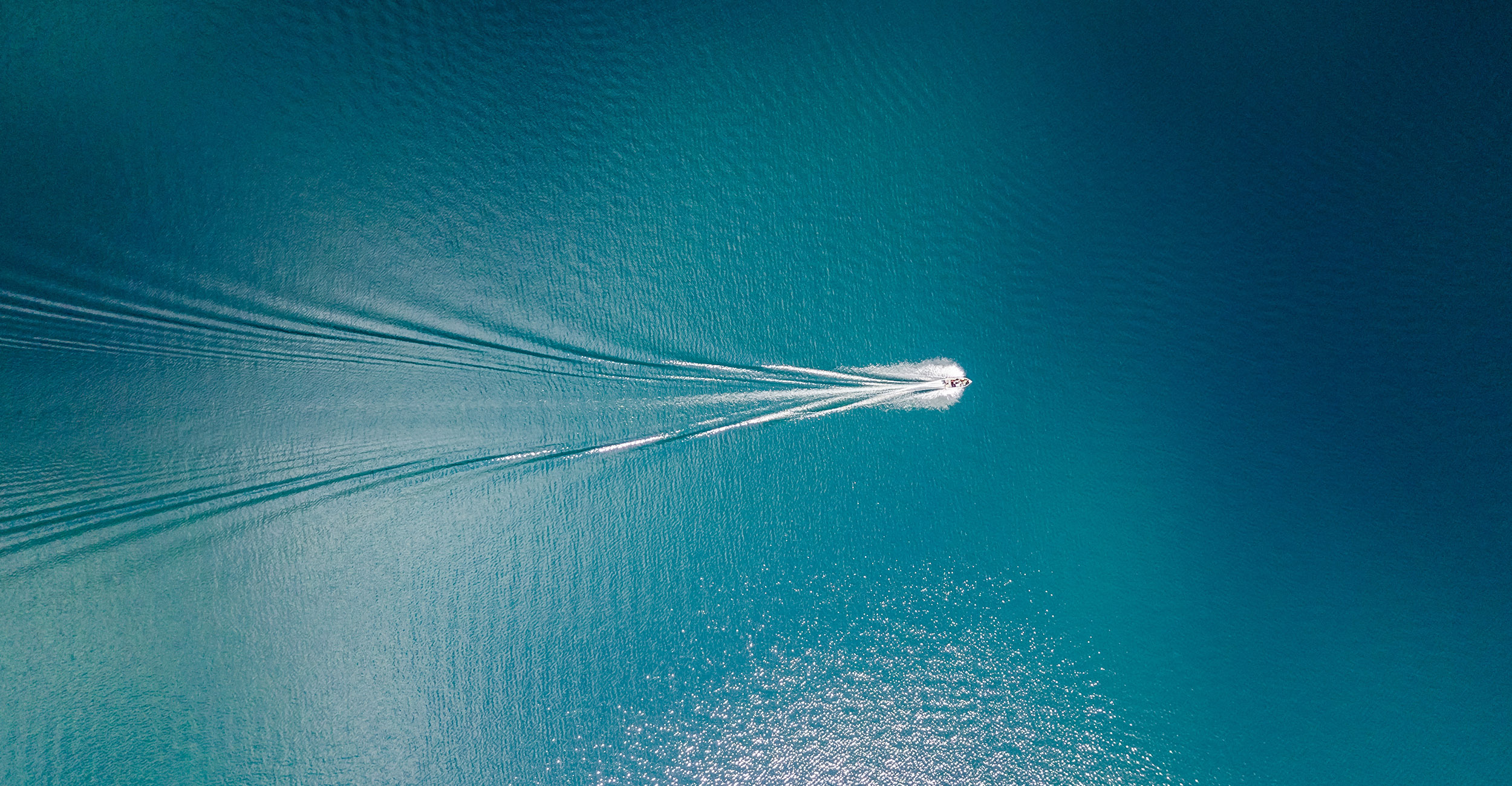 Aerial view of boat sailing across clear blue waters